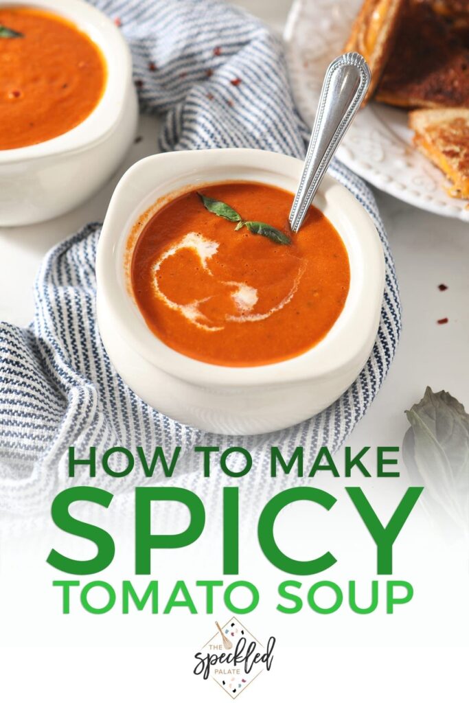 A bowl of tomato soup with a swirl of cream and basil leaves sits on a blue striped towel with the text 'how to make spicy tomato soup'