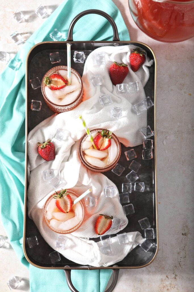 Three glasses of pink tea with strawberry garnishes in a metal tray