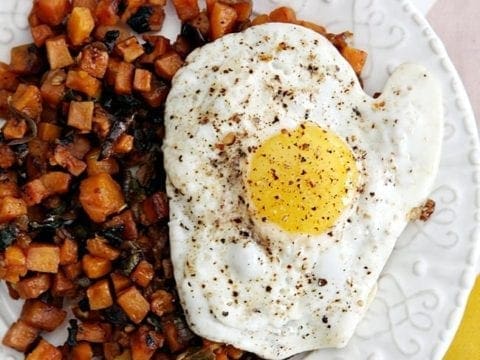 Potato hash and fried egg on white plate