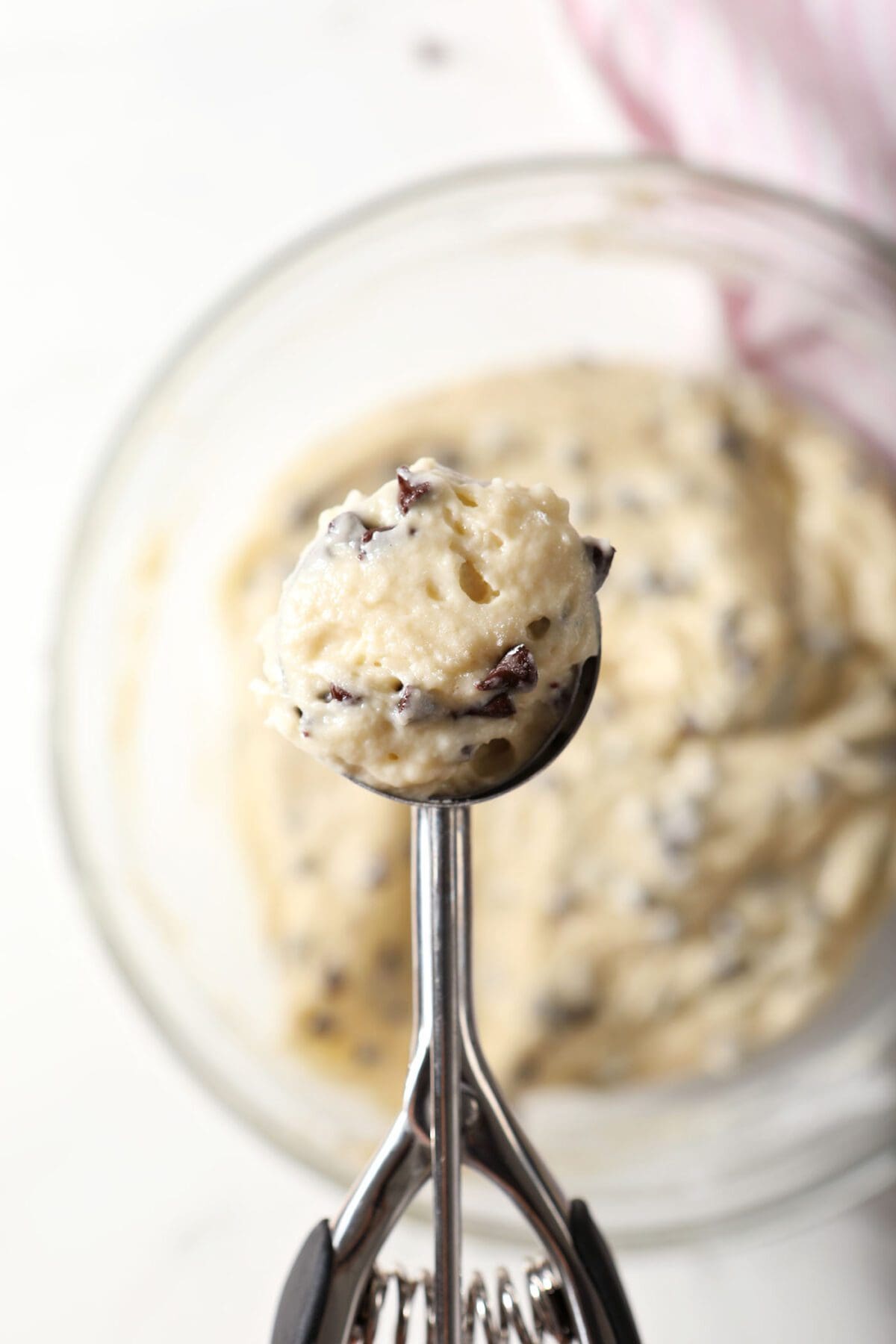 A scoop holds a scoop of chocolate chip muffin batter above a bowl of batter