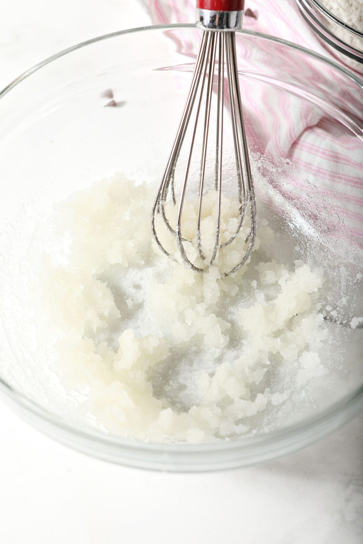 A whisk whisks sugar and oil together in a bowl