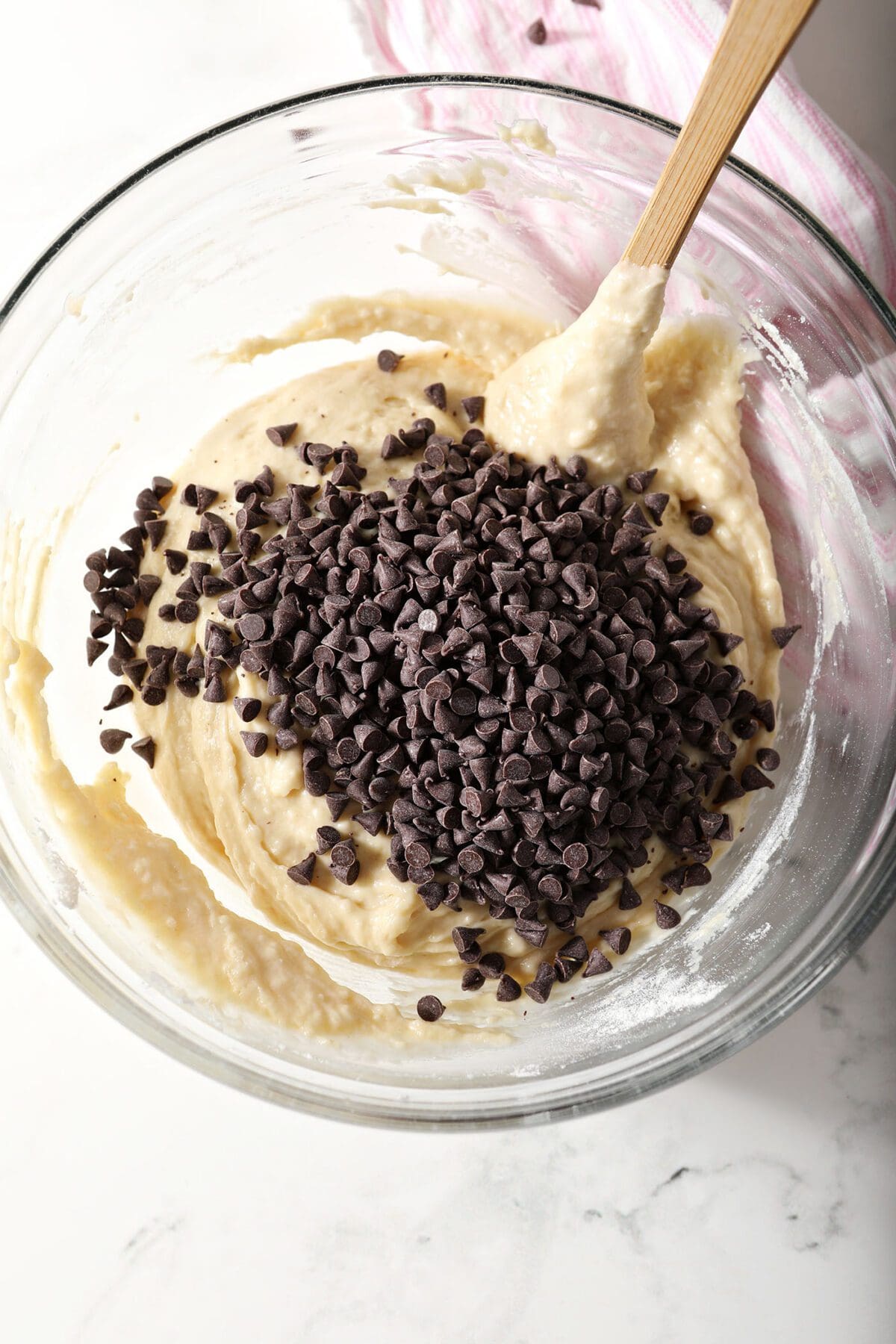 Chocolate chips on top of muffin batter in a bowl with a rubber spatula