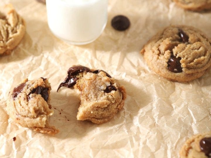 Cookies, fresh out of the oven, are shown on brown paper with shot glasses of milk