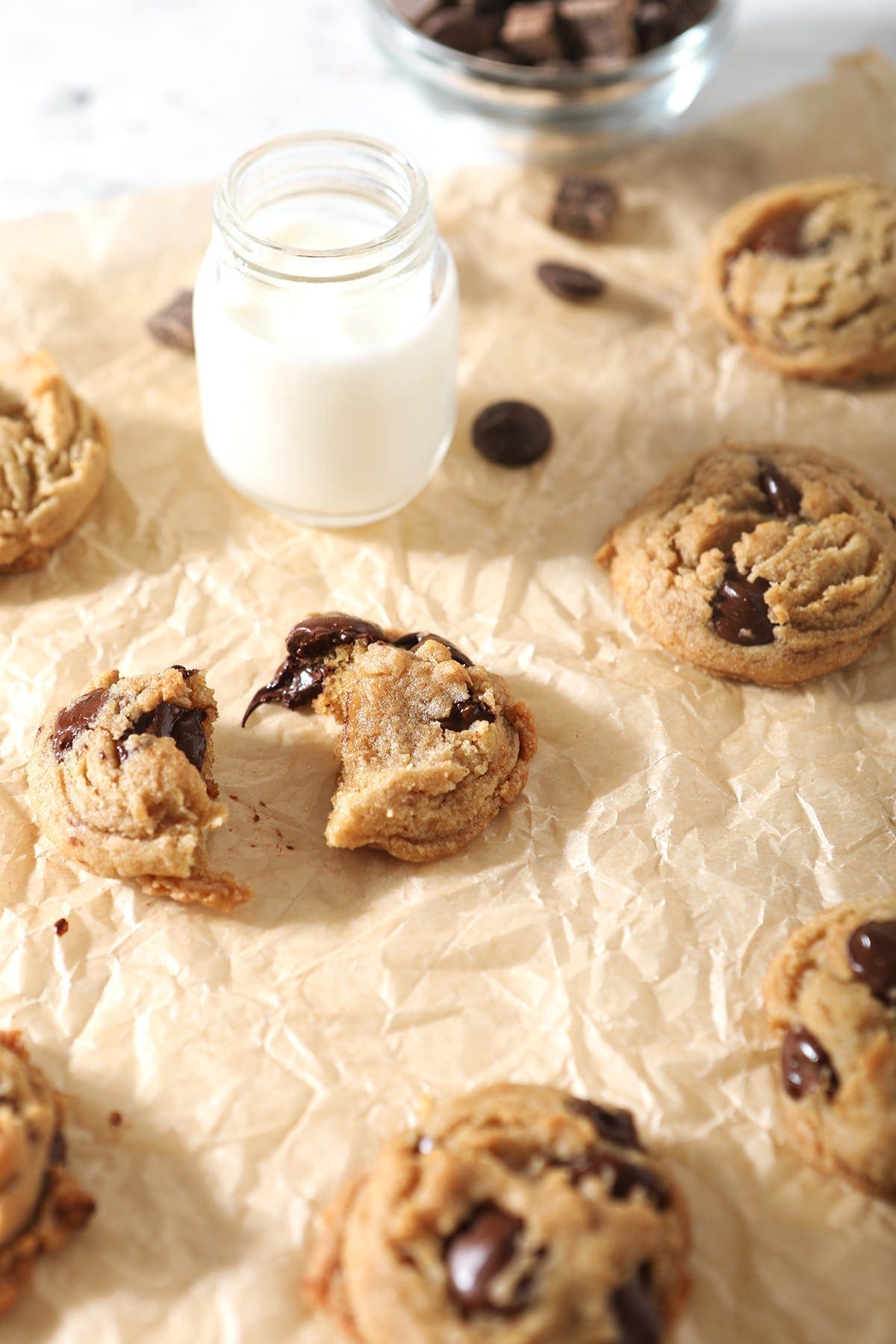 Cookies, fresh out of the oven, are shown on brown paper with shot glasses of milk