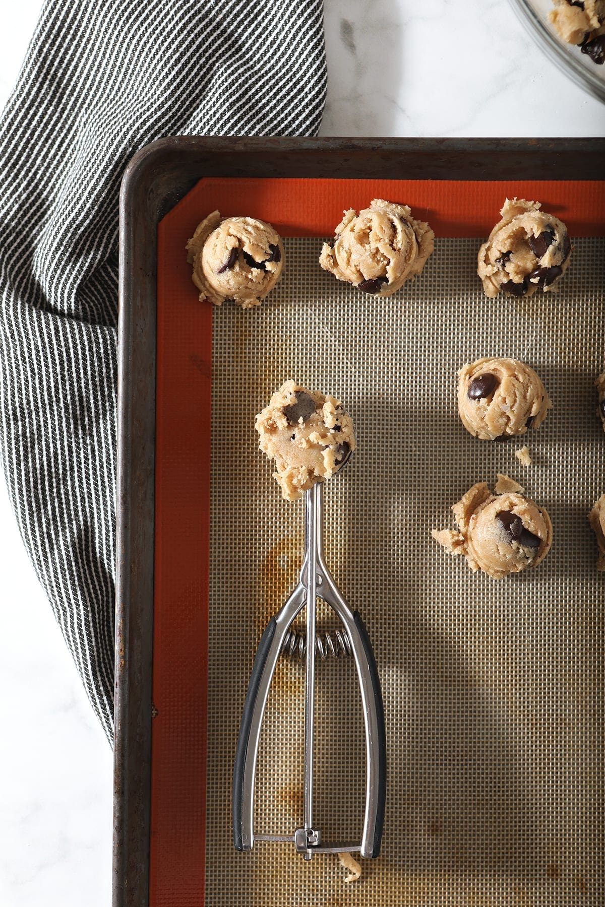 A cookie scoop has some cookie dough inside it, as it scoops cookies onto a prepared baking sheet