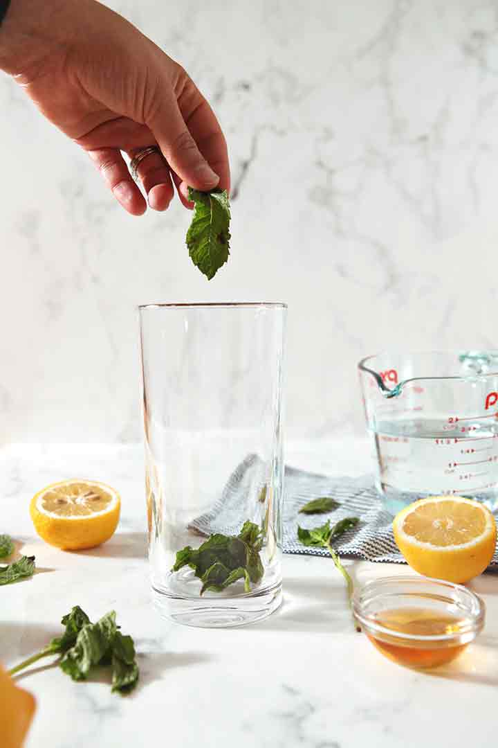 A woman drops a mint leaf into a glass