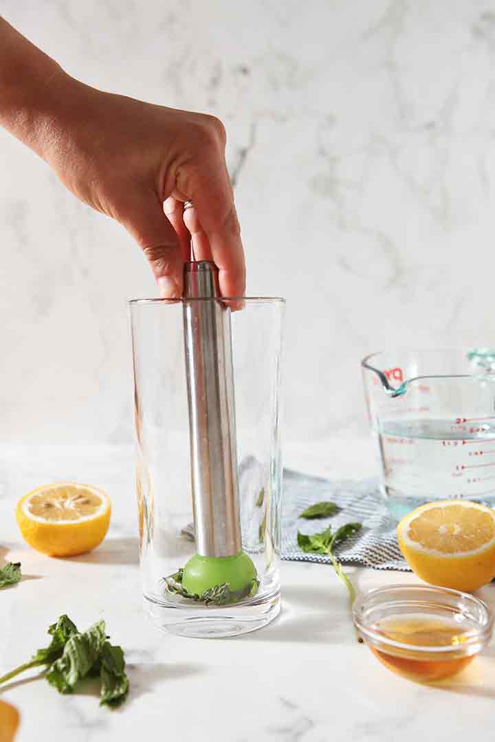 A woman muddles mint in a glass