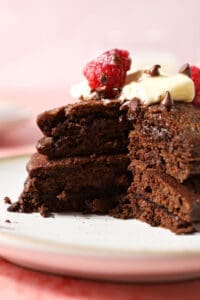 Close up of a sliced into stack of chocolate pancakes topped with a pat of butter, mini chocolate chips and raspberries