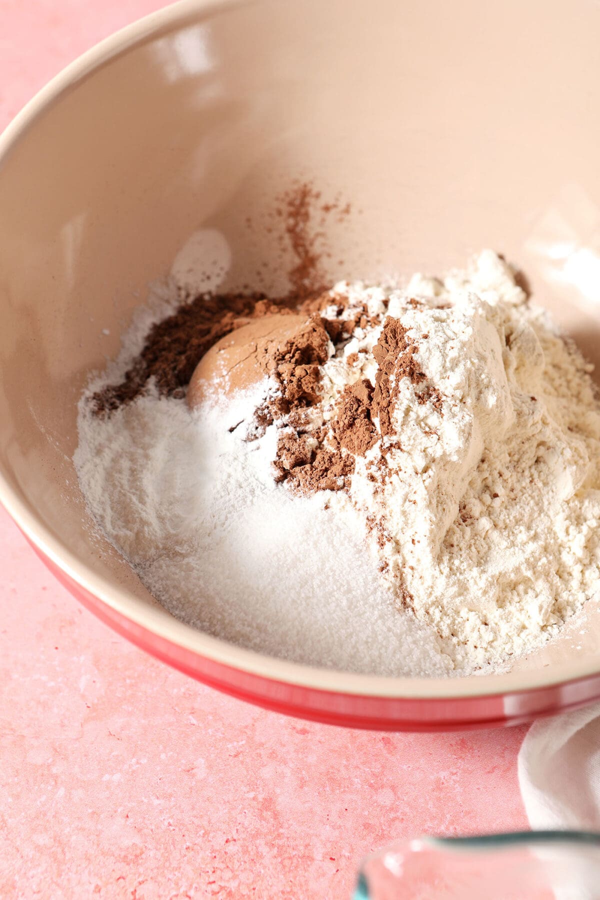 Dry ingredients to make chocolate pancakes in a large bowl on a pink surface