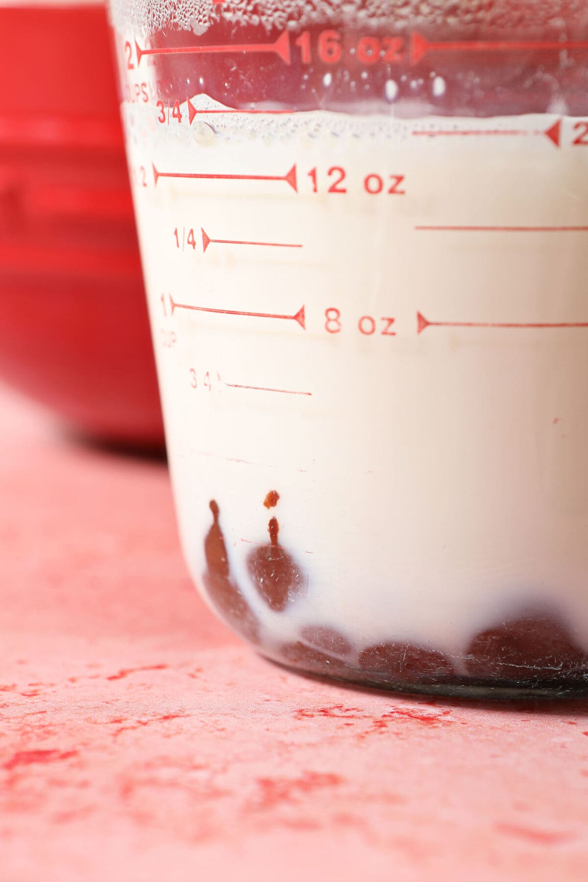 Melted chocolate chips in milk in a liquid measuring cup on a pink surface