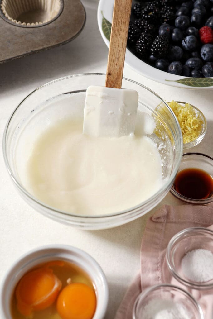 Sour cream and oil, mixed, in a bowl surrounded by other bowls of muffin ingredients