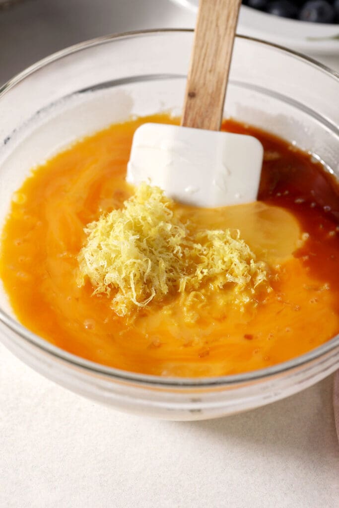 Eggs, lemon zest and vanilla in a bowl with a rubber spatula and other wet ingredients