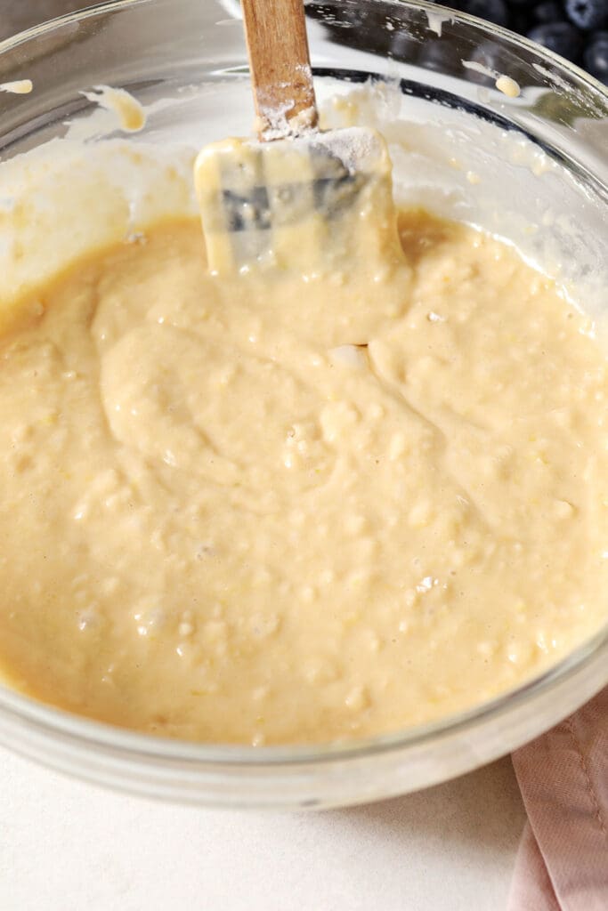 Muffin batter in a bowl with a rubber spatula on a white surface with a pink linen