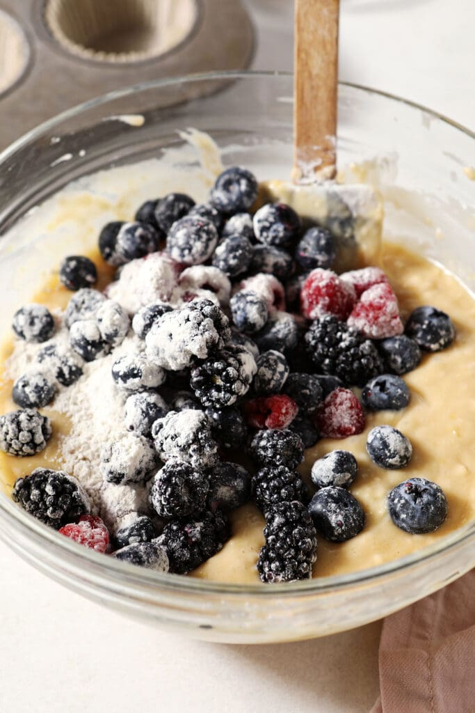 Berries tossed in flour on top of muffin batter in a bowl