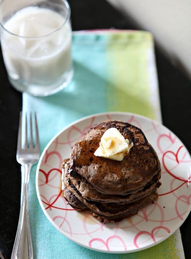 Stack of pancakes on plate with fork and glass of milk