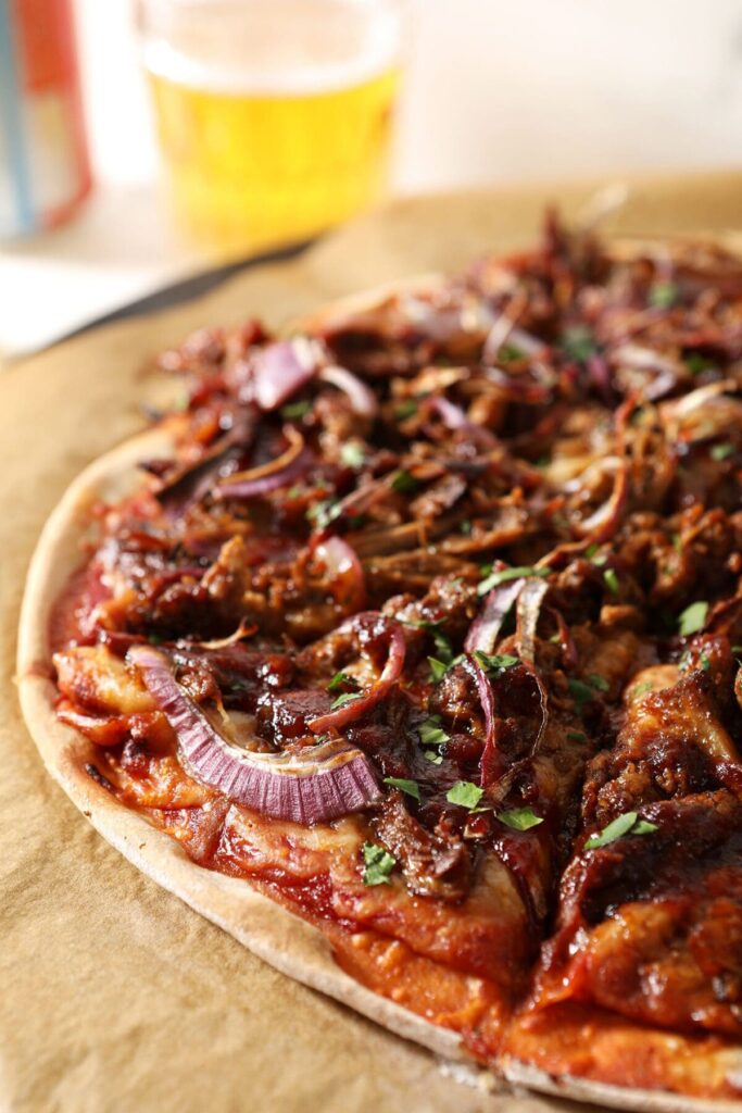 Sliced bbq pizza on a pizza stone with beer