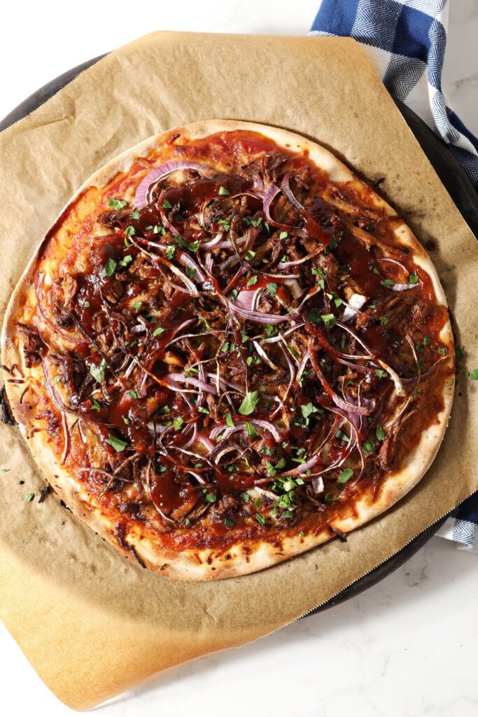 A round bbq pulled pork pizza garnished with cilantro on a pizza stone