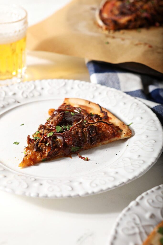 A slice of bbq pizza on a white plate next to a beer