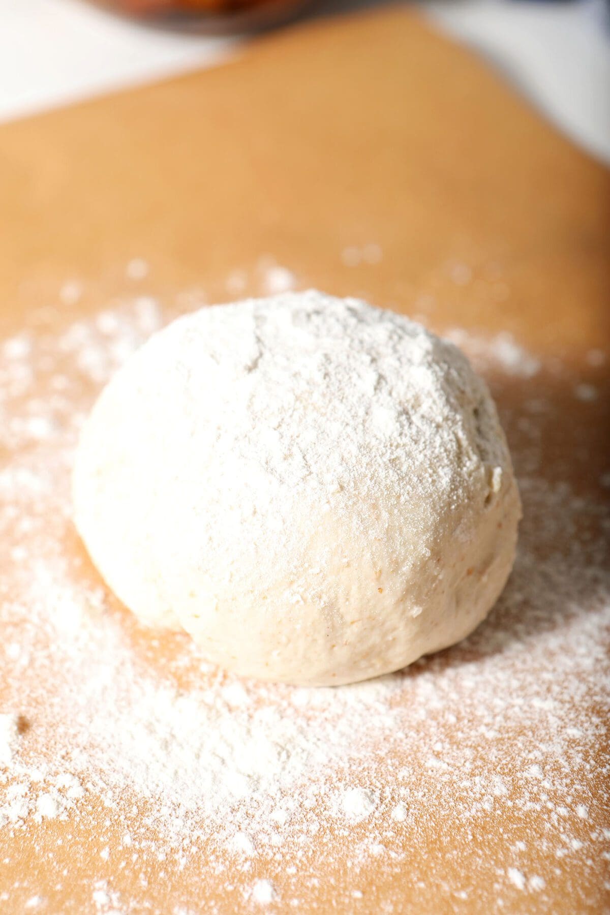 A round of pizza dough on a sheet of brown parchment paper