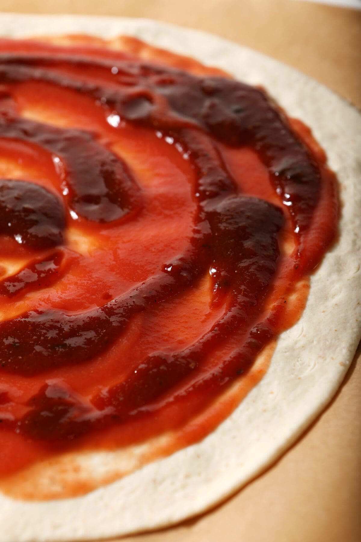 BBQ sauce swirls into tomato sauce on a round of pizza dough