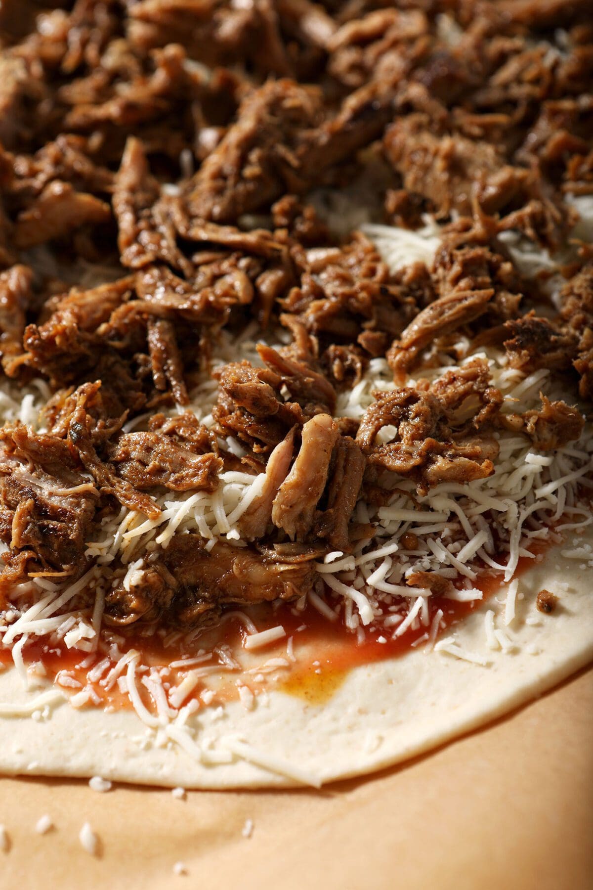 Close up of pulled pork on top of shredded cheese on a pizza