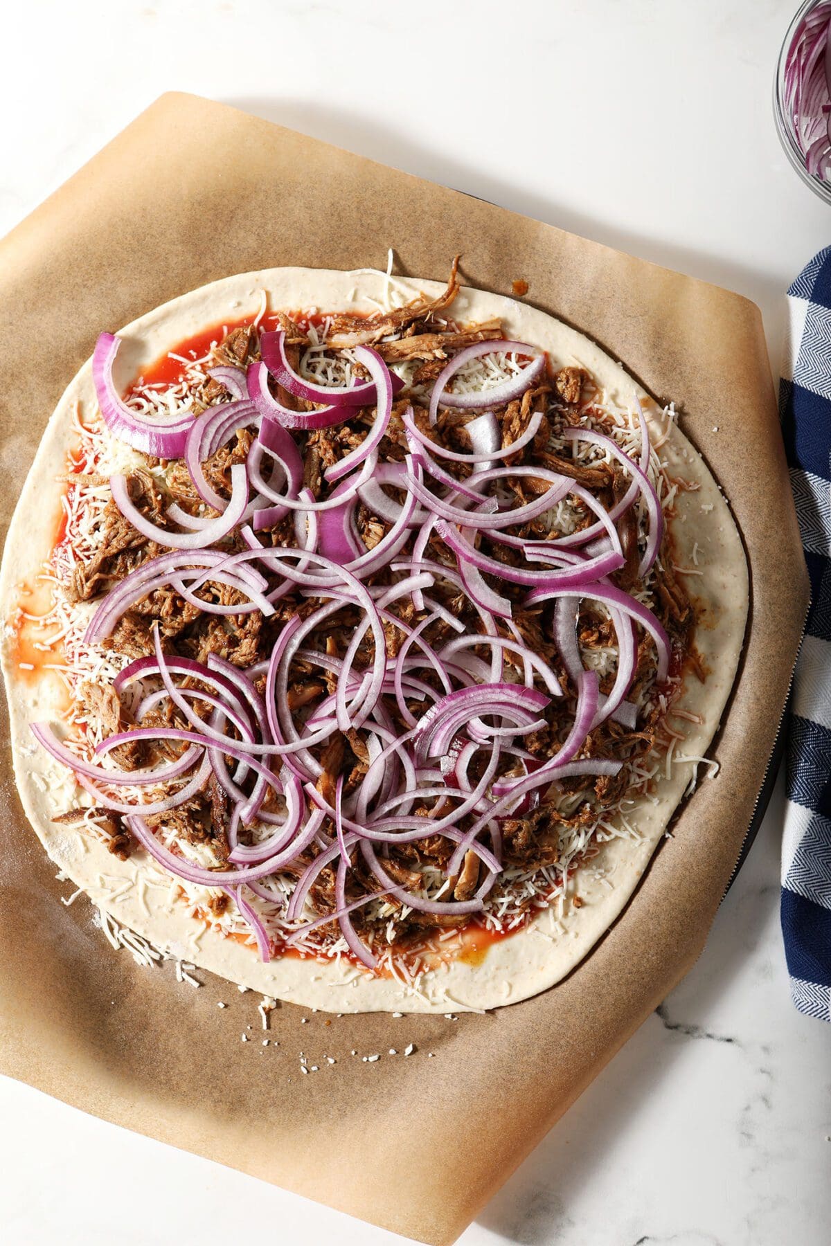 Red onion rings on top of pulled pork on a pizza before baking