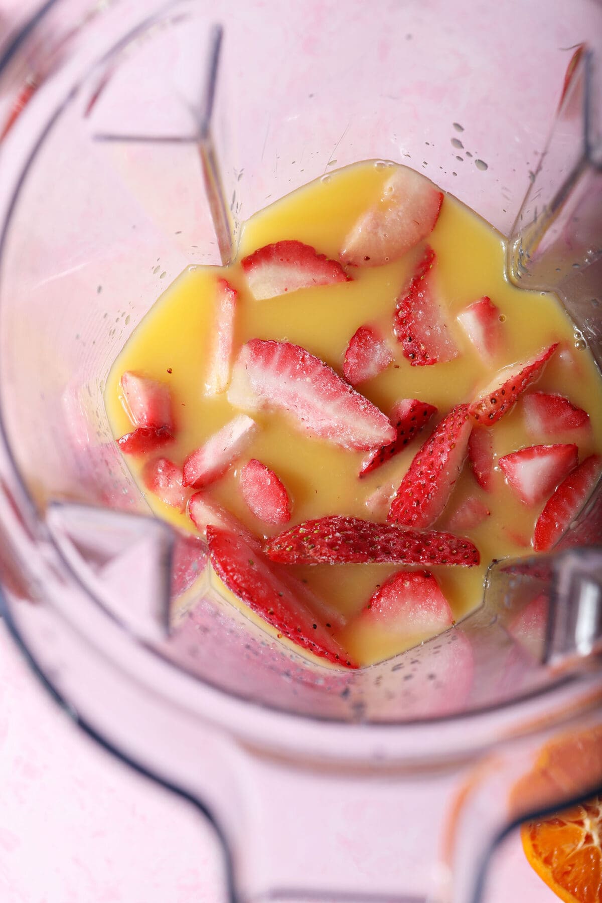 frozen strawberry slices and orange juice in the base of a blender before blending