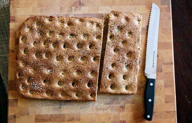 Sliced focaccia bread on a wooden cutting board next to knife 