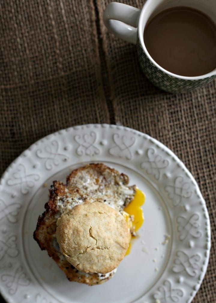Overhead view of breakfast sandwich on plate next to cup of coffee