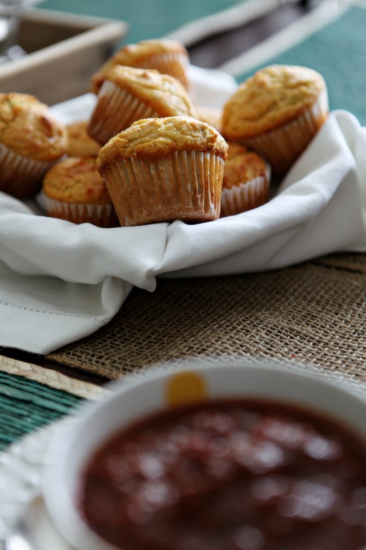 A basket holds a serving of Honey Jalapeño Cornbread Muffins, perfectly paired with a bowl of chili, shown in the foreground