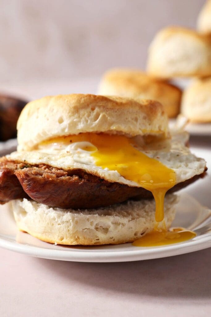 Egg yolk drops off a biscuit sandwich with boudin on a white plate