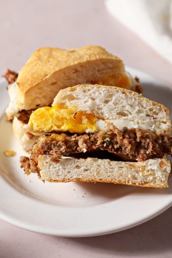 A halved biscuit sandwich with boudin and a jammy egg on a white plate