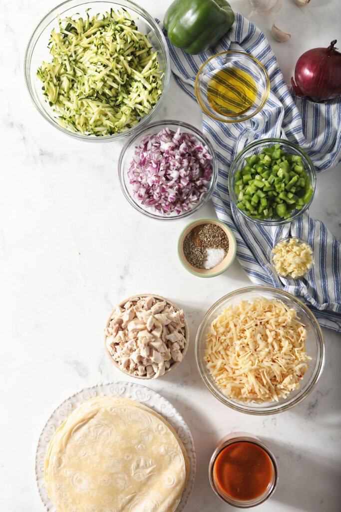 Ingredients to make Zucchini Chicken Enchiladas in bowls on marble