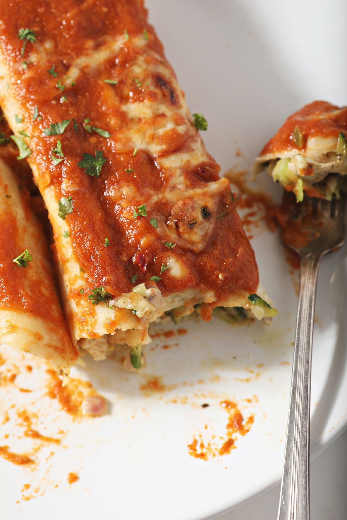 Close up of a plate of zucchini chicken enchiladas with a fork and a bite taken