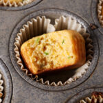 A bitten-into Honey Jalapeno Cornbread Muffin in a tin next to other corn muffins