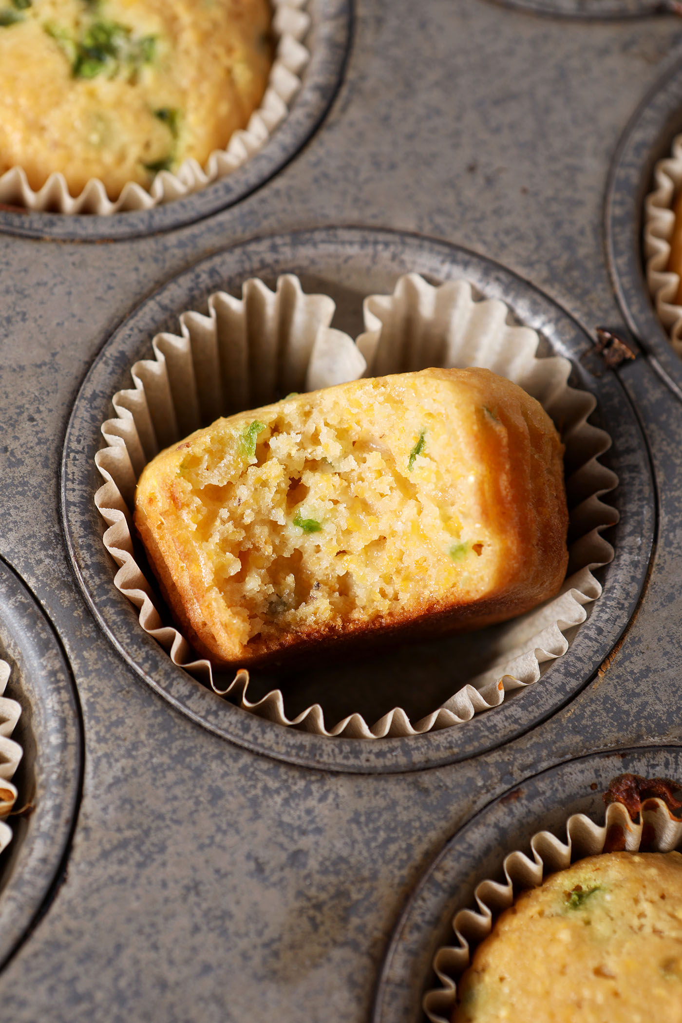 A bitten-into Honey Jalapeno Cornbread Muffin in a tin next to other corn muffins