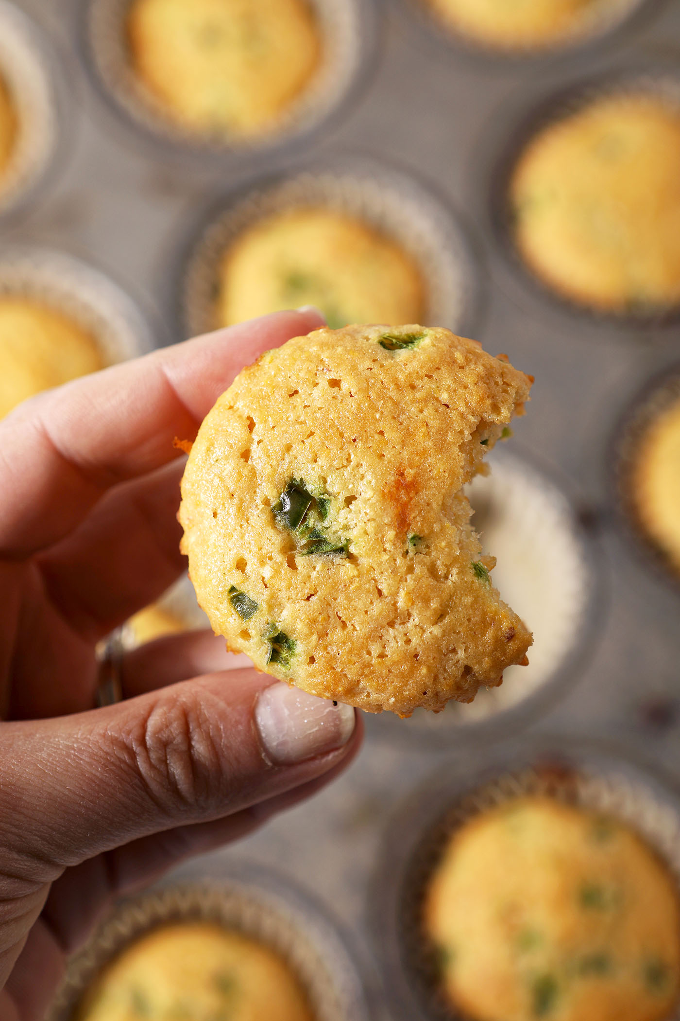 A bitten-into Jalapeno Corn Muffin held above a muffin tin with more muffins