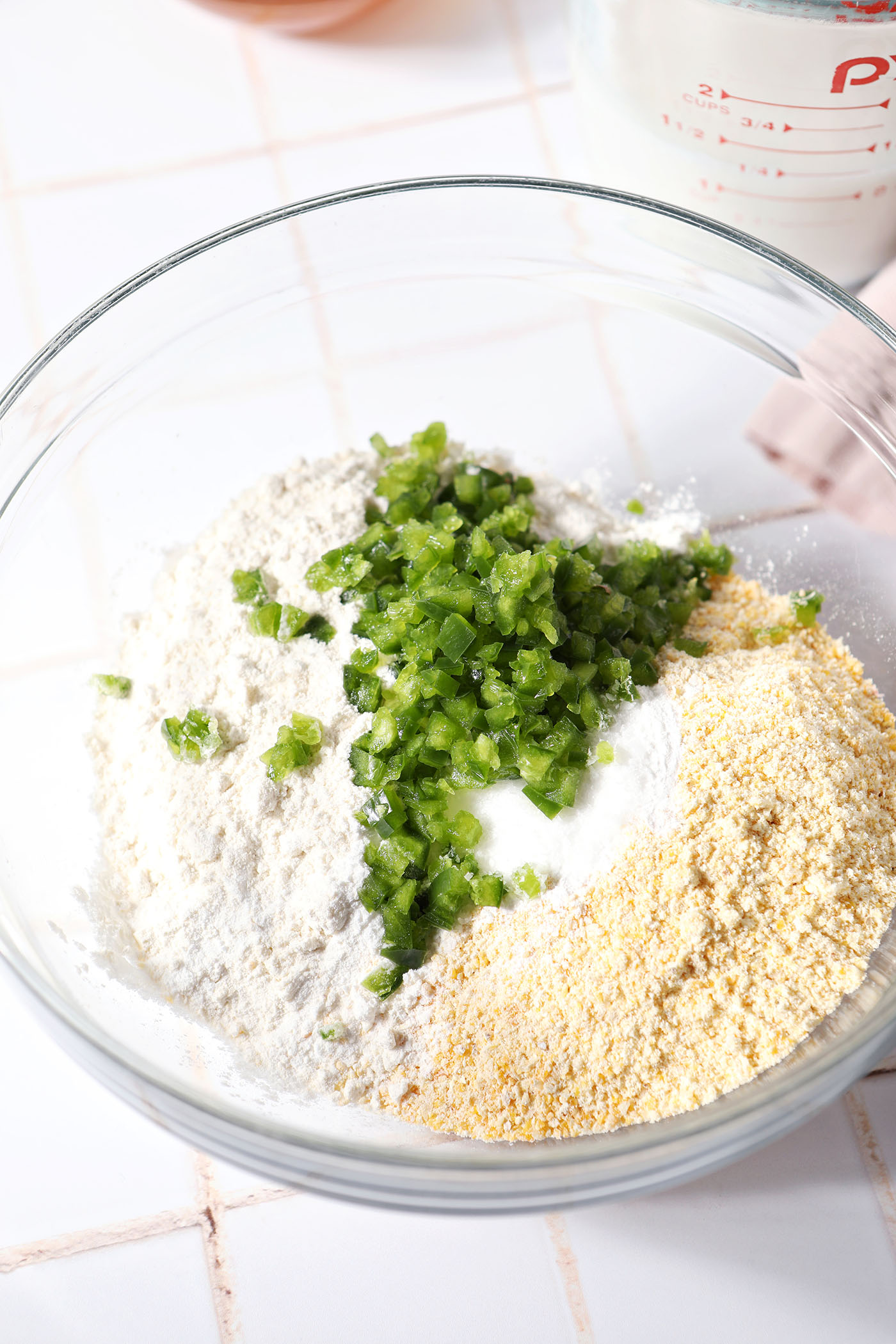 Dry ingredients to make corn muffins with jalapenos in a bowl on a white tiled surface