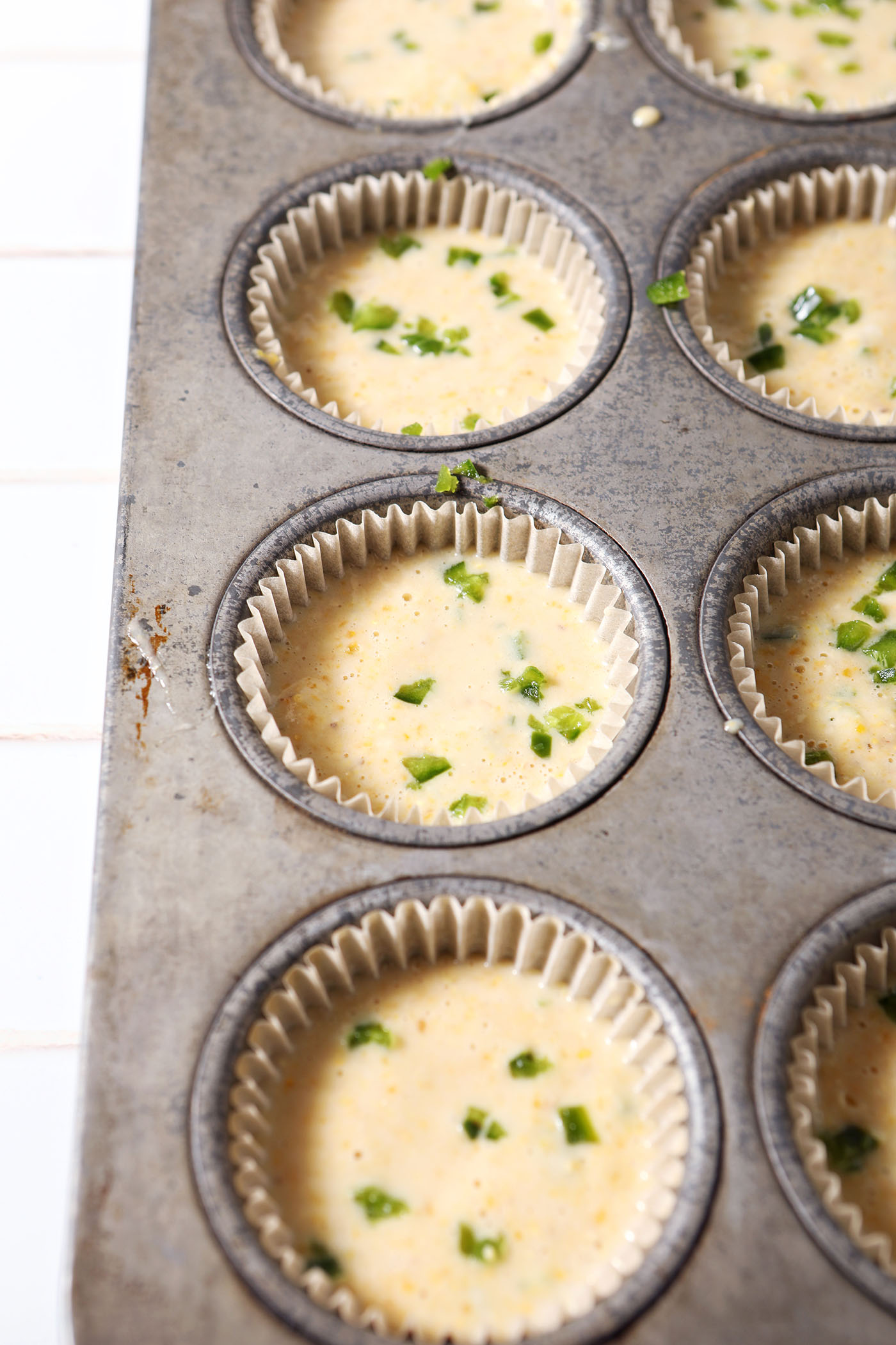 Cornbread muffin batter garnished with chopped jalapeño in a muffin tin before baking