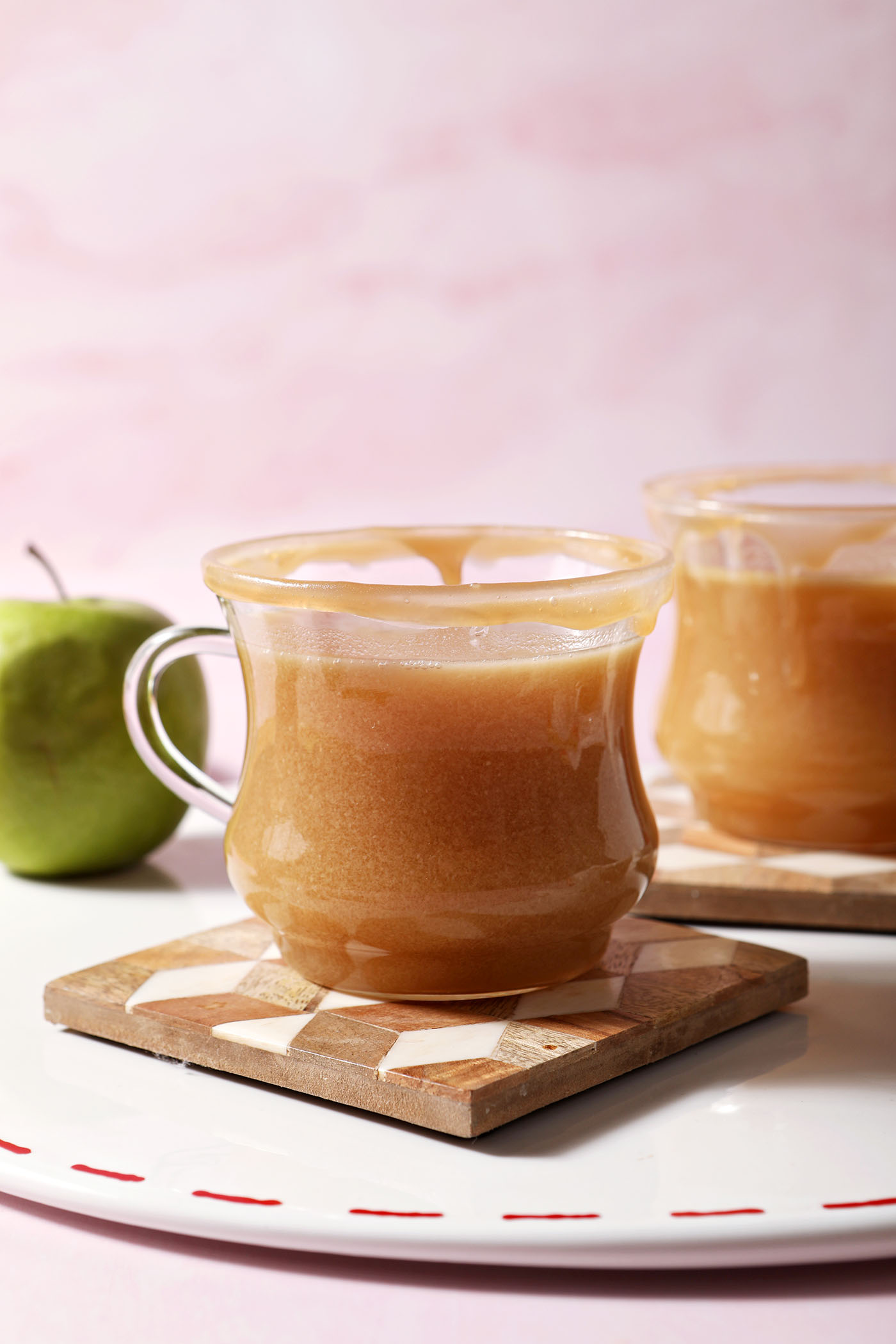 Two glasses of Spiked Caramel Apple Cider on wooden coasters on a white platter