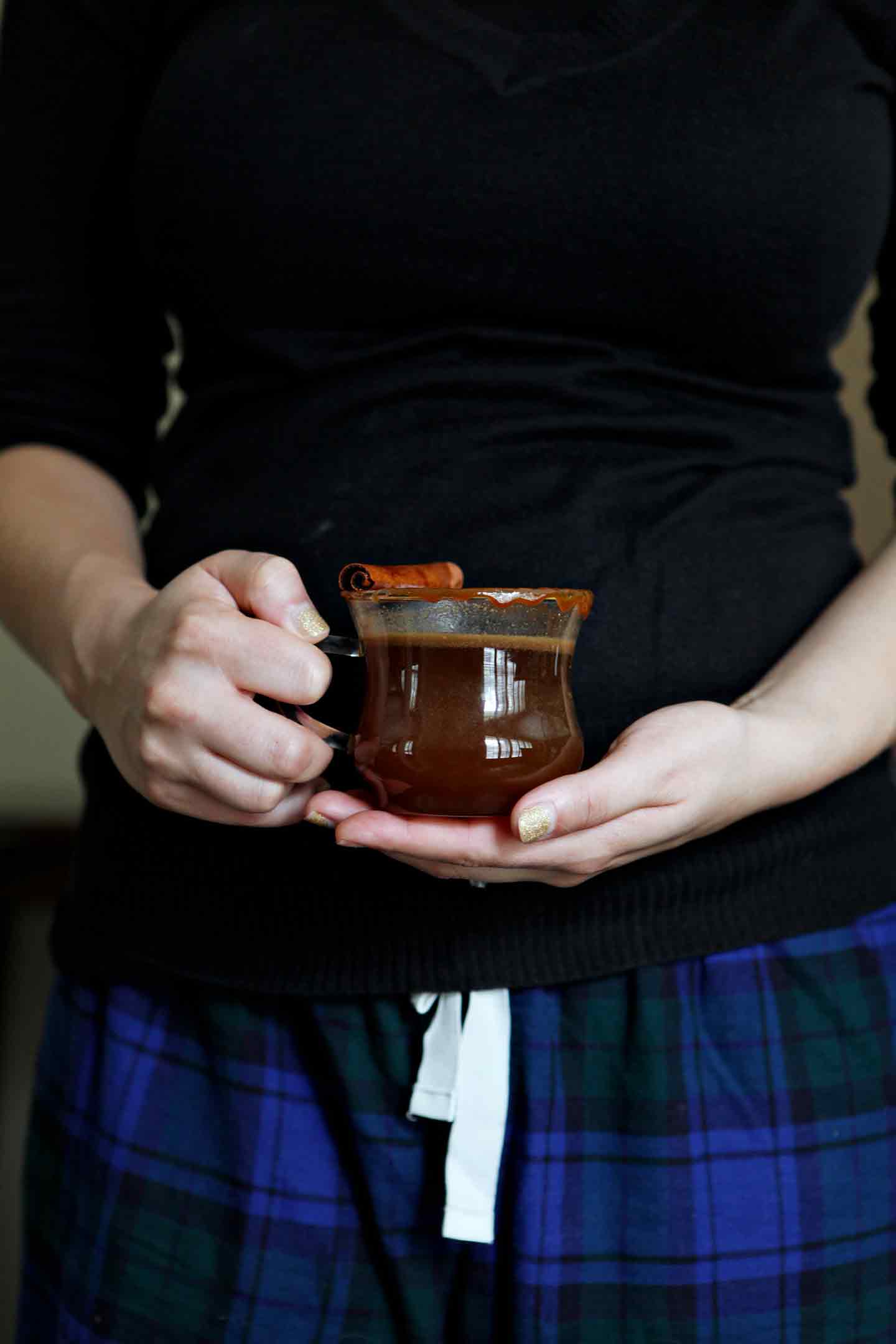 A woman holds a warm glass of Spiked Caramel Apple Cider