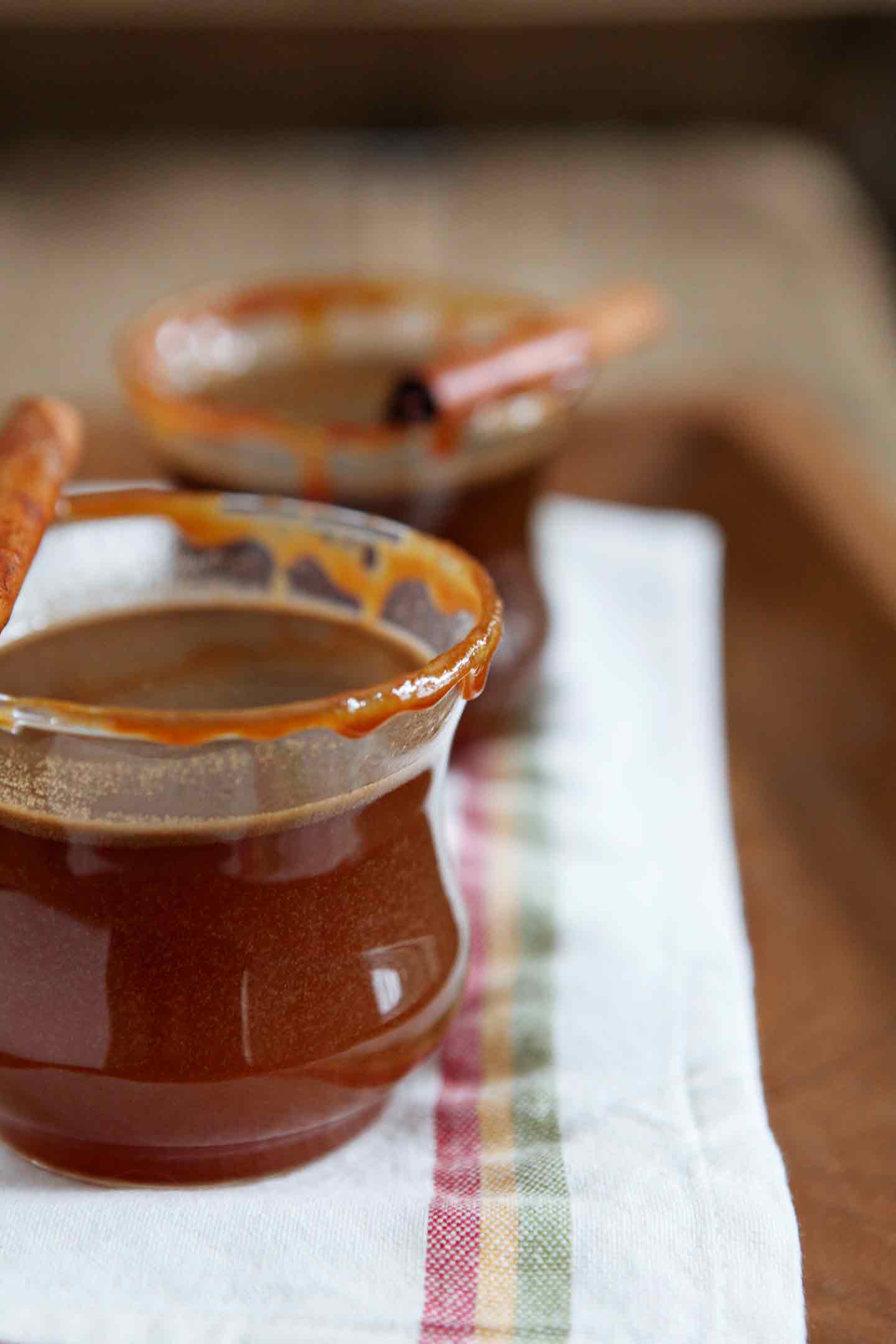 Two glasses of Spiked Apple Cider are served on a wooden serving tray