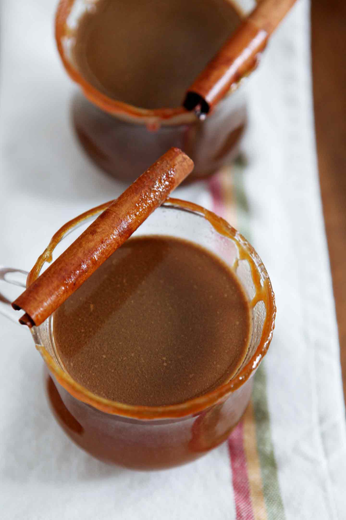 Two glasses of Spiked Apple Cider sit on a wooden serving tray