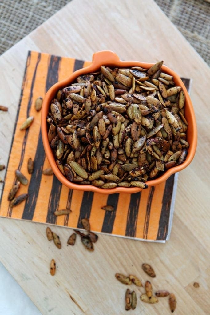 Roasted Pumpkin Seeds are displayed in a pumpkin-shaped bowl on a wooden background