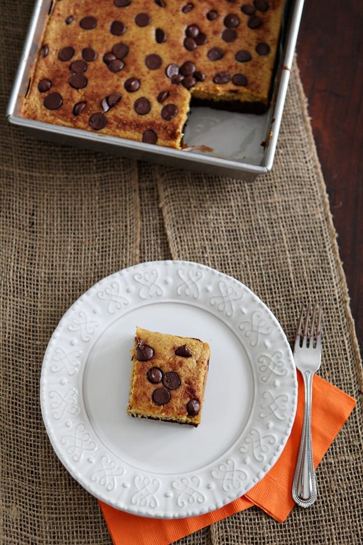 A white plate holds a pumpkin bar next to a fork and the pan holding the rest of the brownies