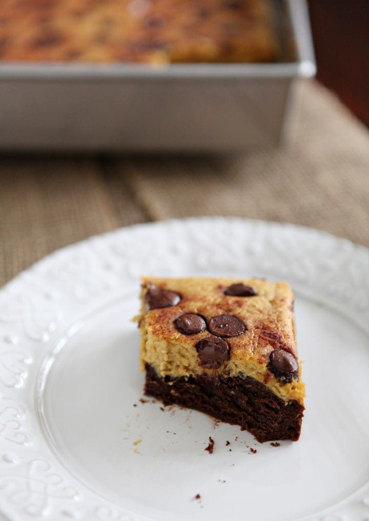 Close up of a pumpkin cheesecake bar on a white platter that's been cut into with a baking pan behind it on a tabletop