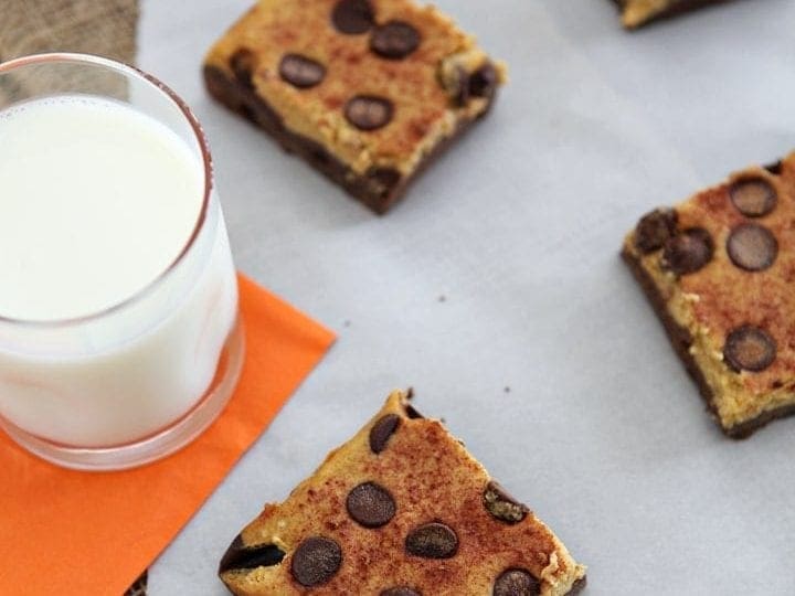 Pumpkin Cheesecake Brownie Bars are served on parchment paper with a glass of milk