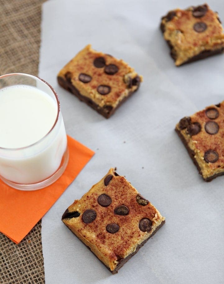 Pumpkin Cheesecake Brownie Bars are served on parchment paper with a glass of milk