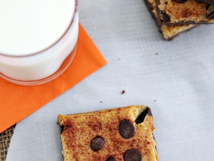 Overhead closeup of pumpkin cheesecake bars on a white piece of parchment with a glass of milk