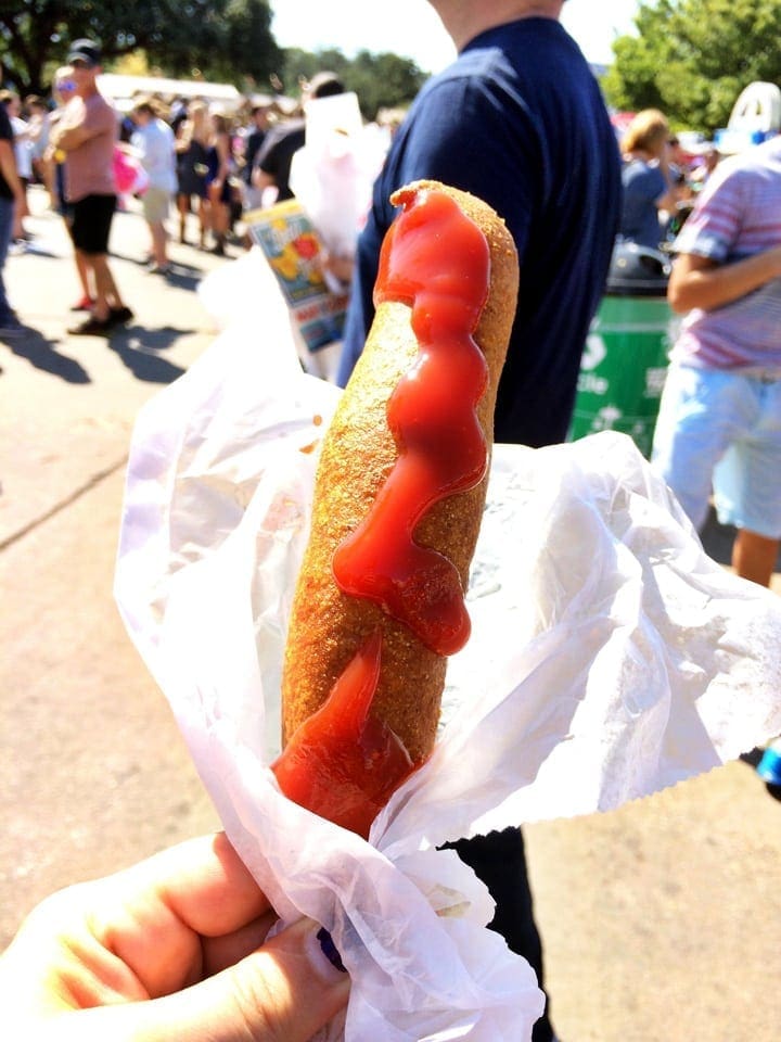 Person holding a hot dog with ketchup running down on a stick  